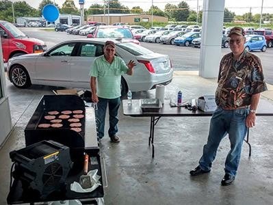 Two men grilling burgers at event.